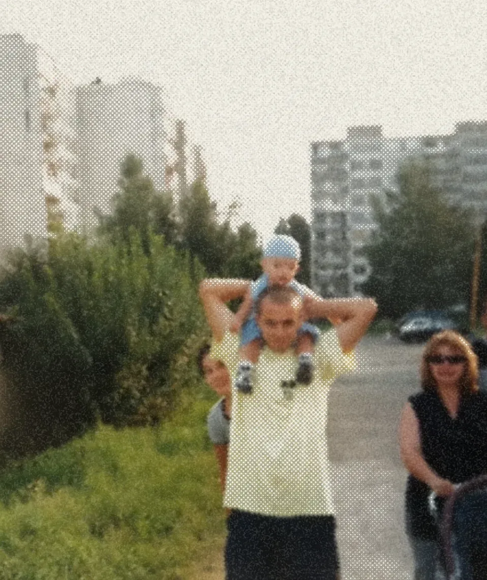 A road between blocks of flats, a small child up on a man’s shoulders and the rest of the family walking behind.