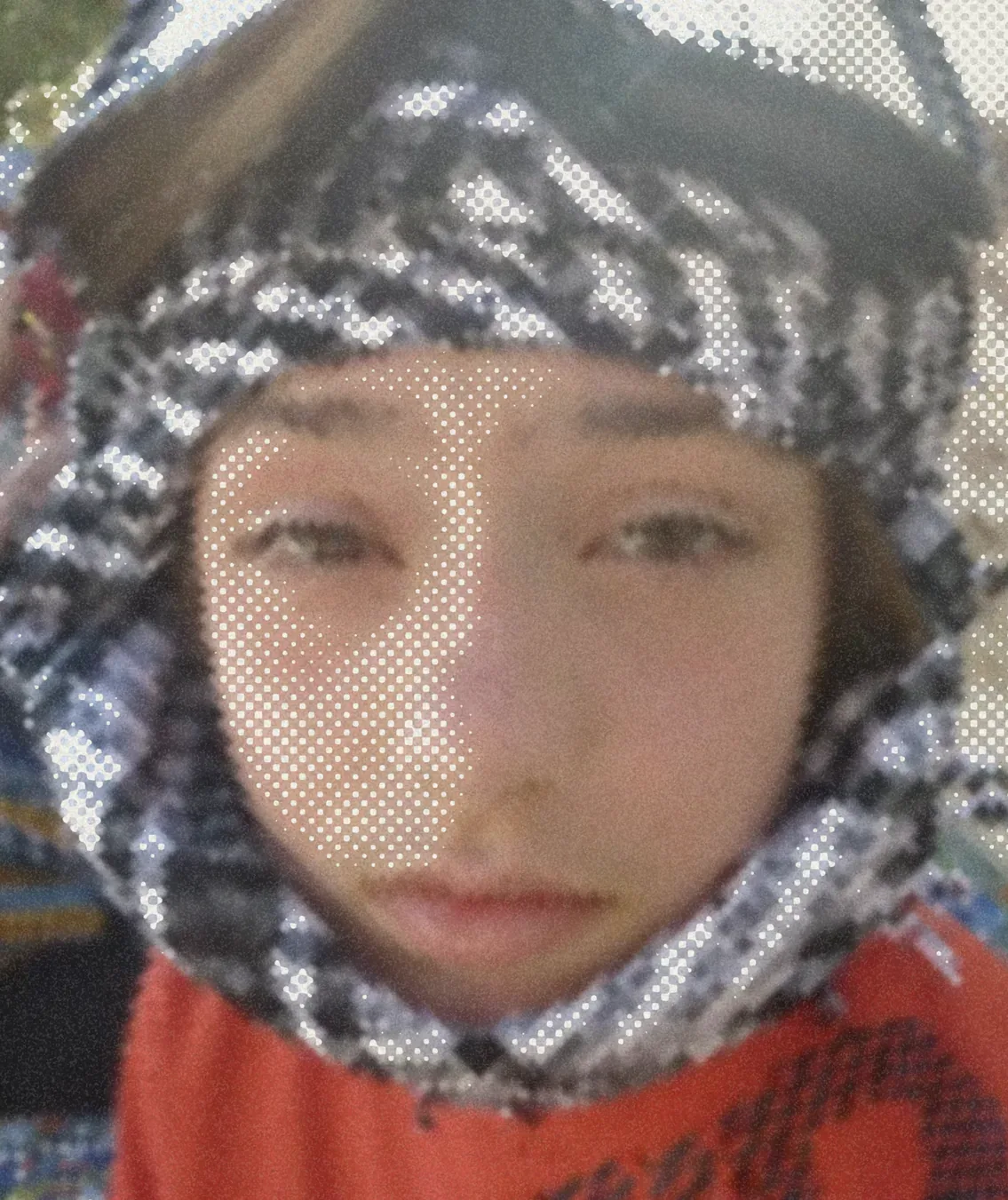 A small child in a patterned winter hood, straight to camera, a street out of focus behind.