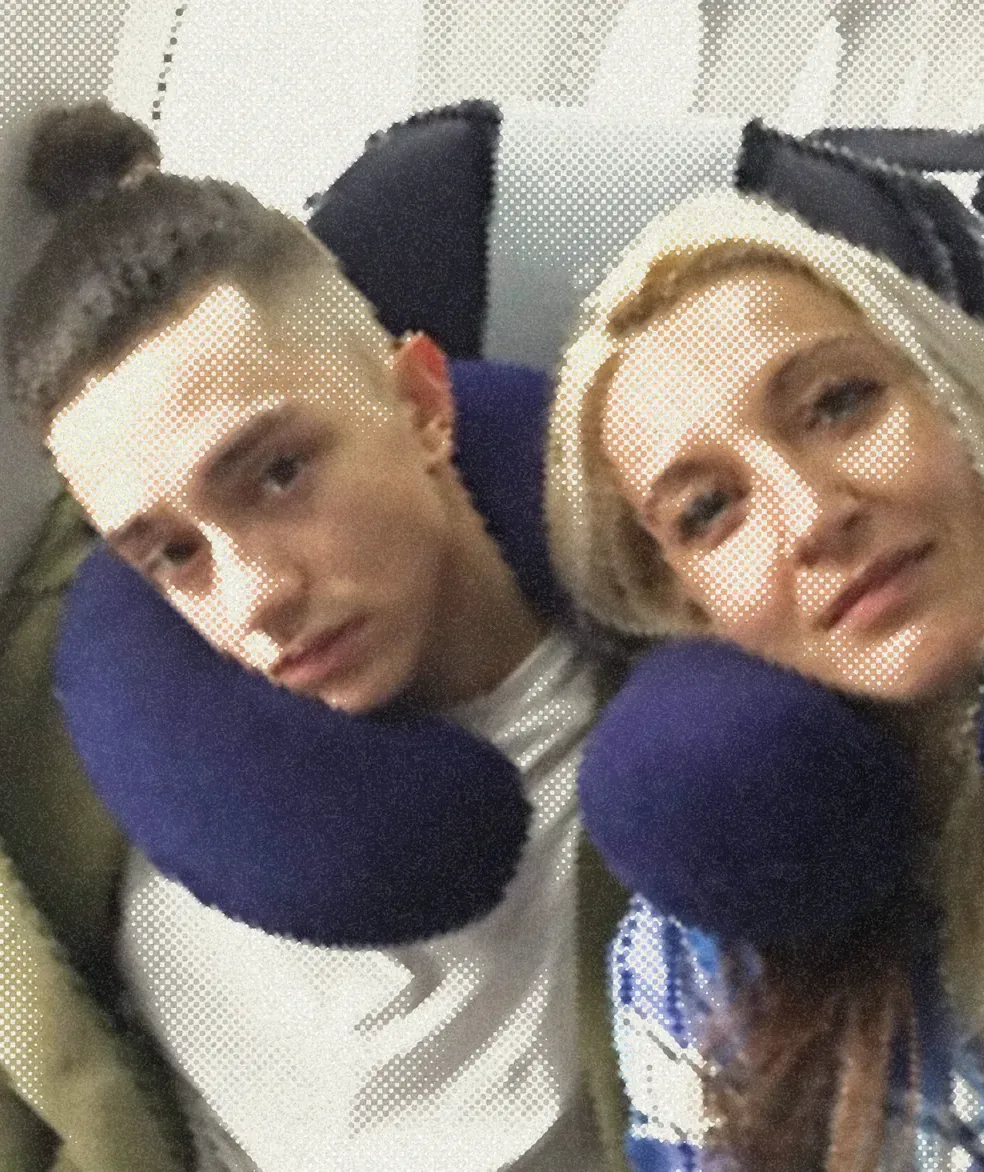 Two people in travel pillows and winter hats, heads tipped together.