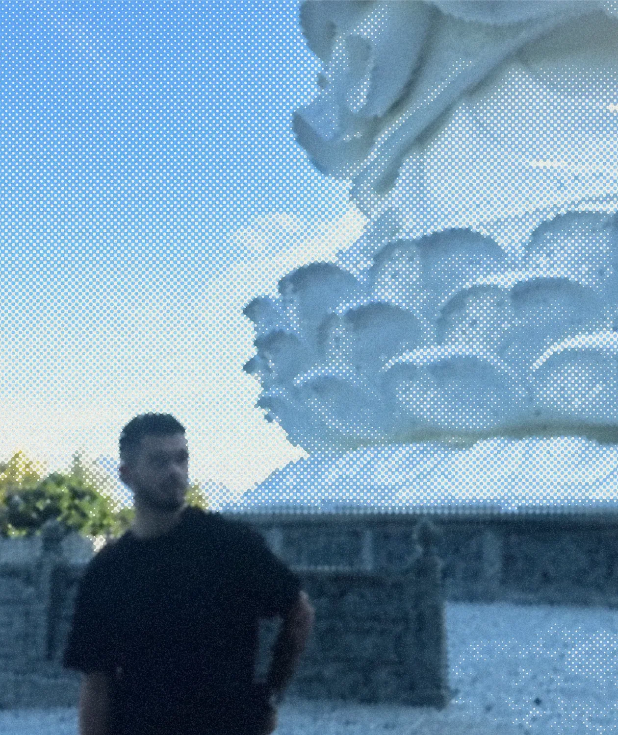 A man in front of a painted wall of clouds running up into a blue sky.